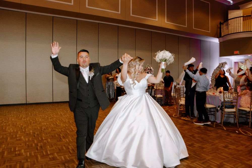 A panoramic view of a wedding reception party dancing on a wooden dance floor in a large banquet hall.