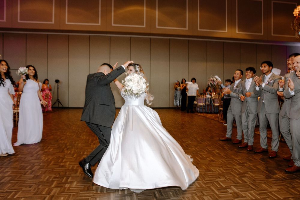Wedding reception dance floor shows guests in gray suits celebrating while watching a ballroom dance performance.
