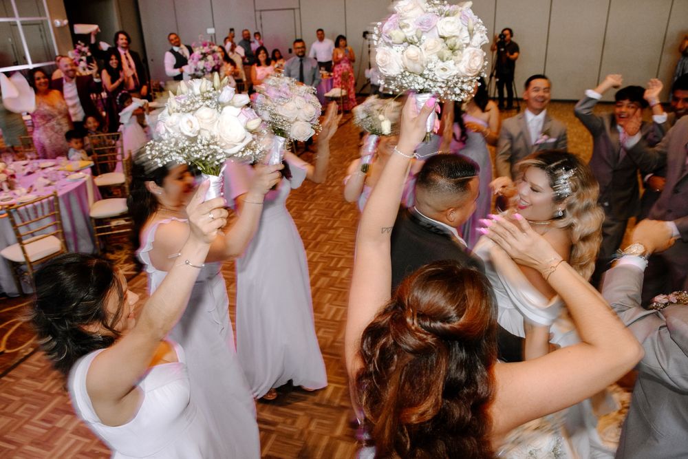 Festive wedding guests dance energetically in a reception hall decorated with soft lighting and floral arrangements.