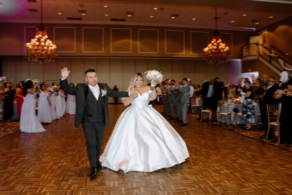 Newlyweds perform their first dance together at a wedding reception in an elegantly lit ballroom with guests watching.