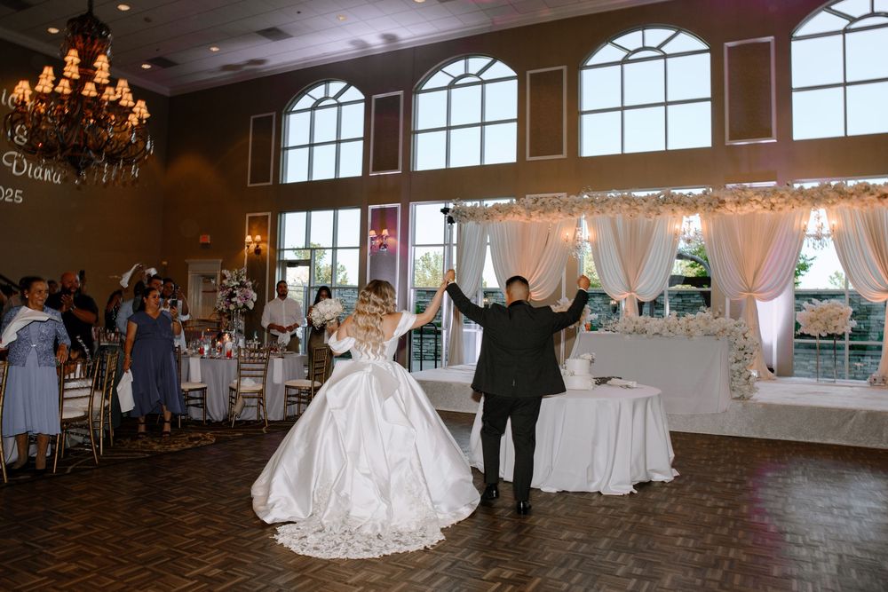 Elegant ballroom setup with arched windows, chandeliers, and white tablecloths creating a romantic wedding reception venue.
