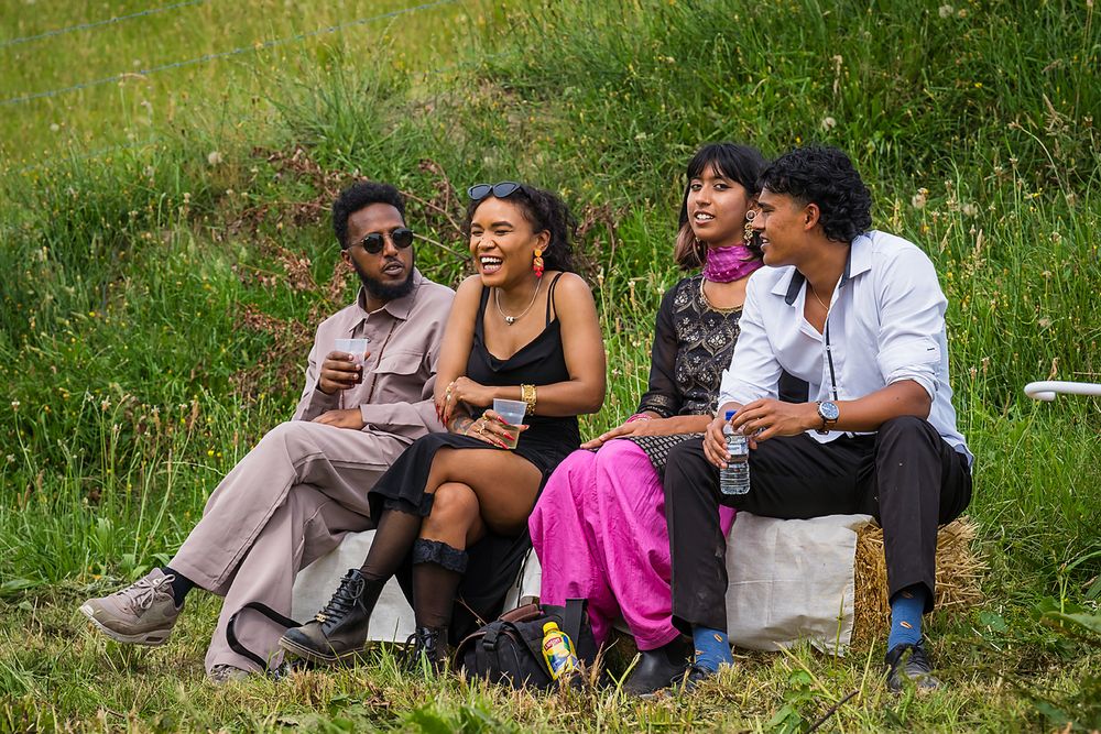Friends relax on grass having conversations and enjoying a sunny afternoon outdoors together.