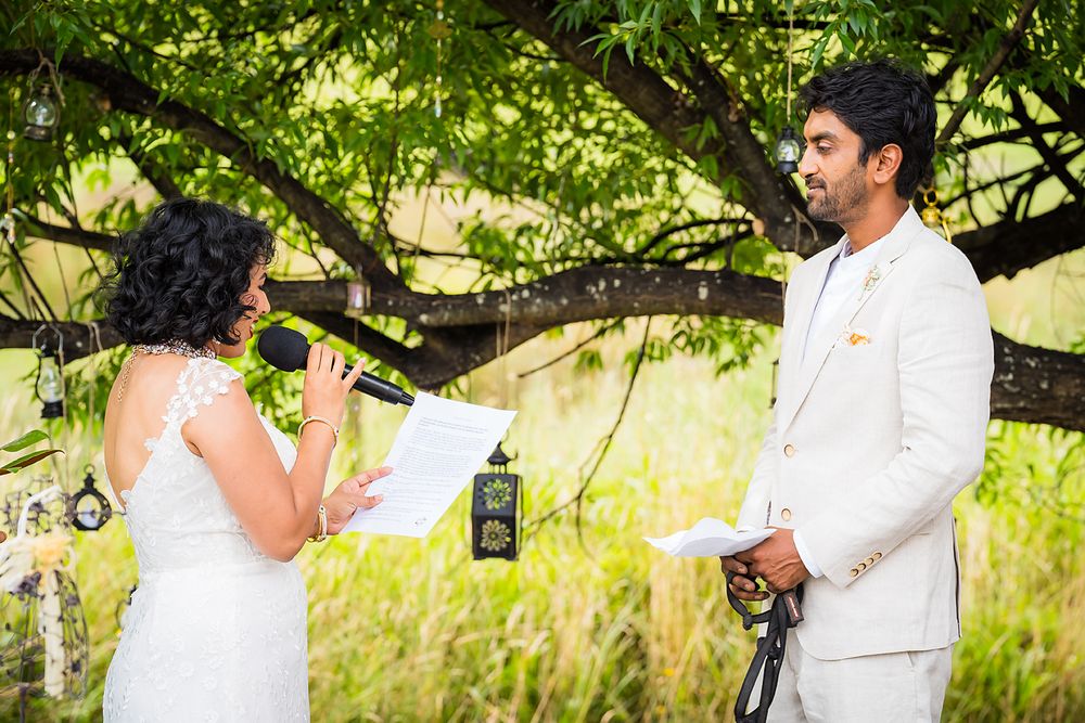 Two people in white outfits dance together under green trees in a romantic outdoor setting.