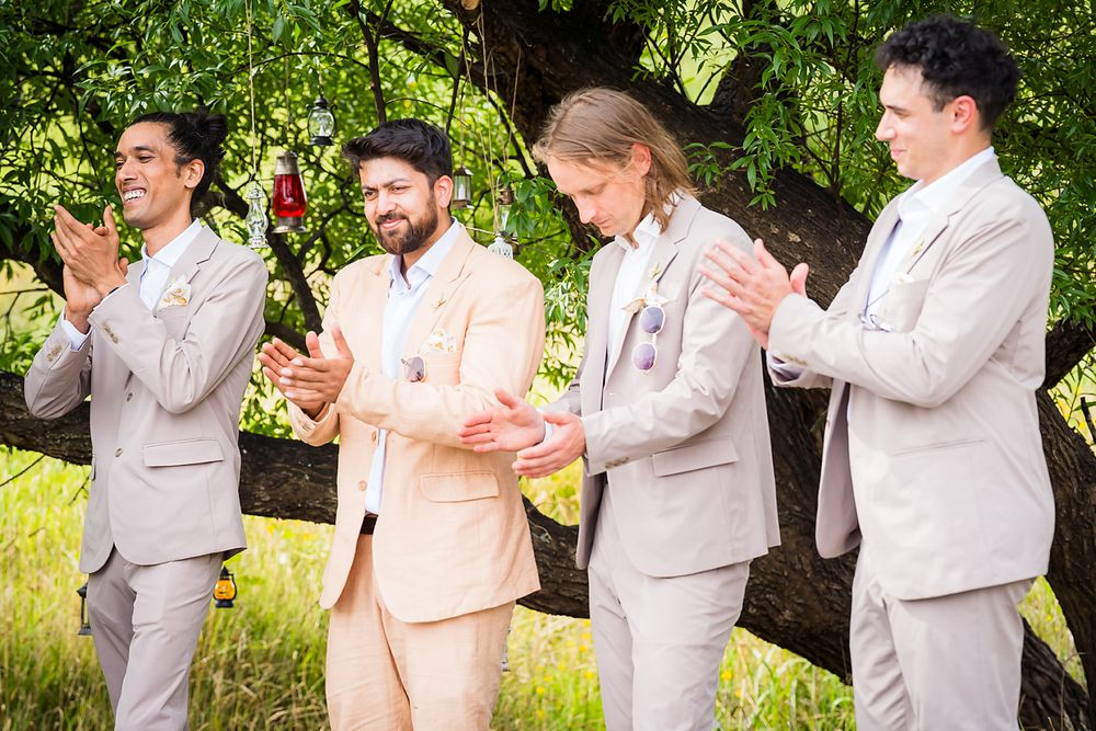 Groomsmen in light gray suits pose playfully in sequence against lush green outdoor backdrop.