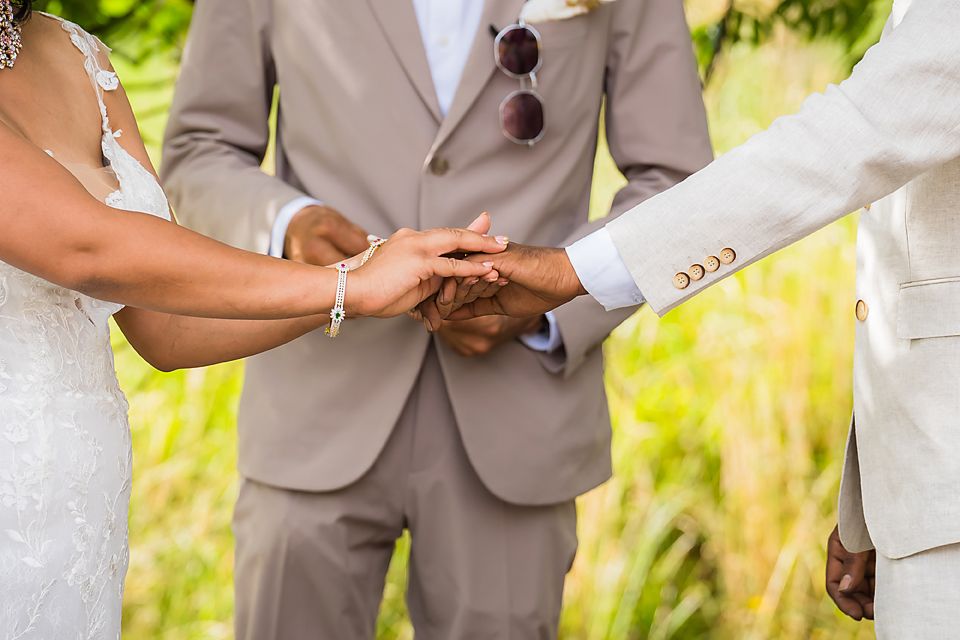 Wedding ceremony couple exchange rings outdoors with their hands held together in tender moment.