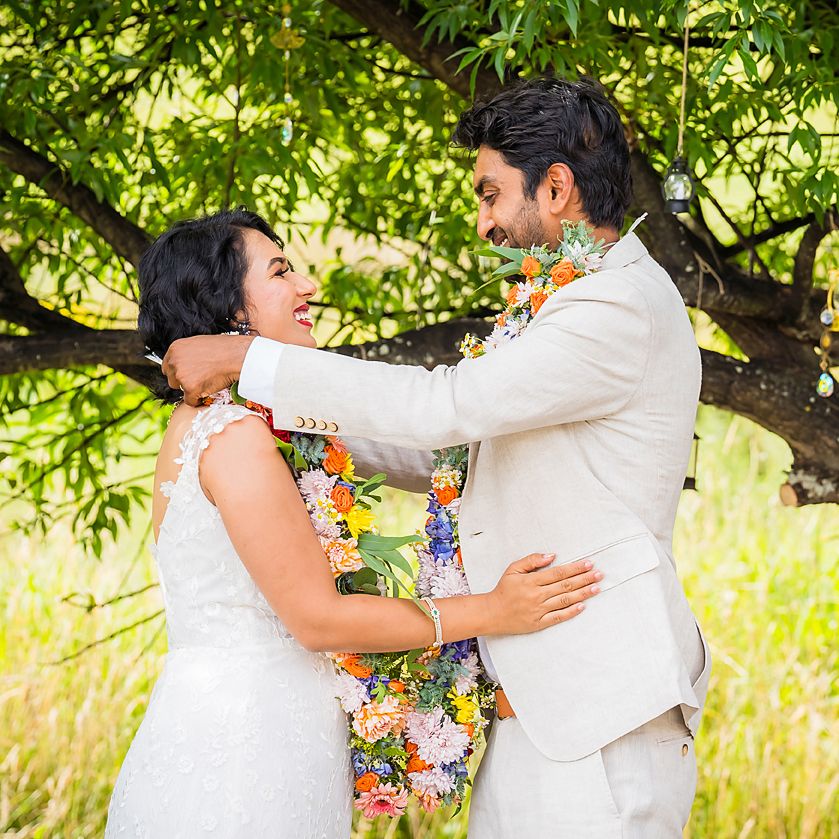 A couple in white wedding attire enjoying a playful candid moment together in a lush garden setting.