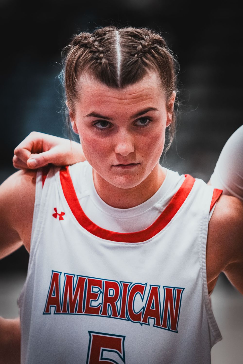 Basketball player in white American jersey with braided hairstyle poses intensely for athletic portrait.