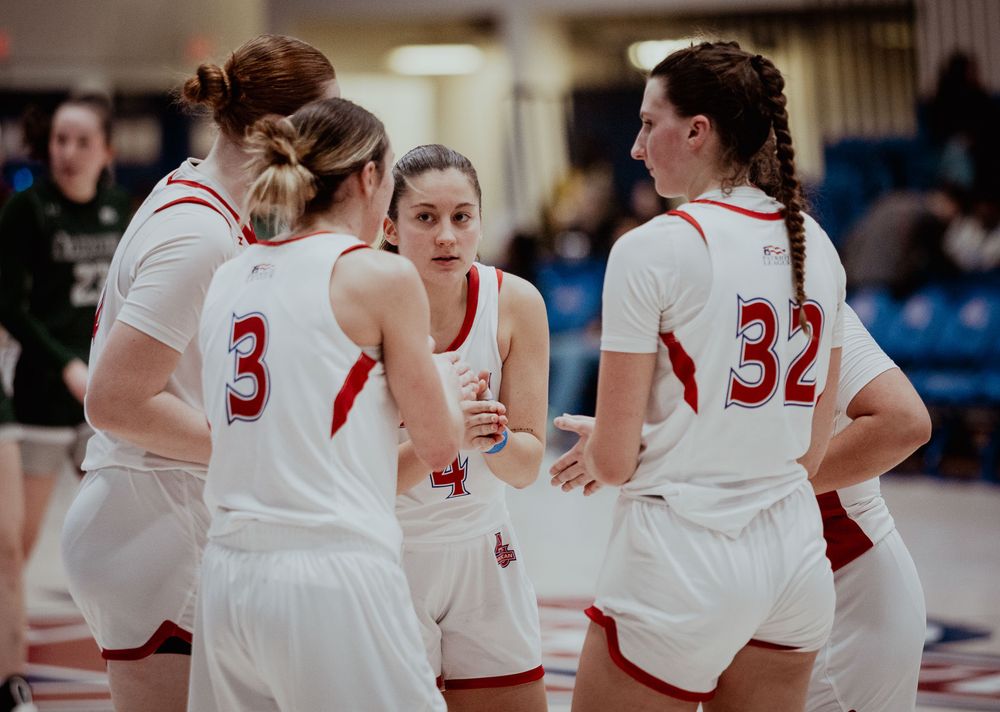 Basketball team huddles together wearing white and red uniforms during game.
