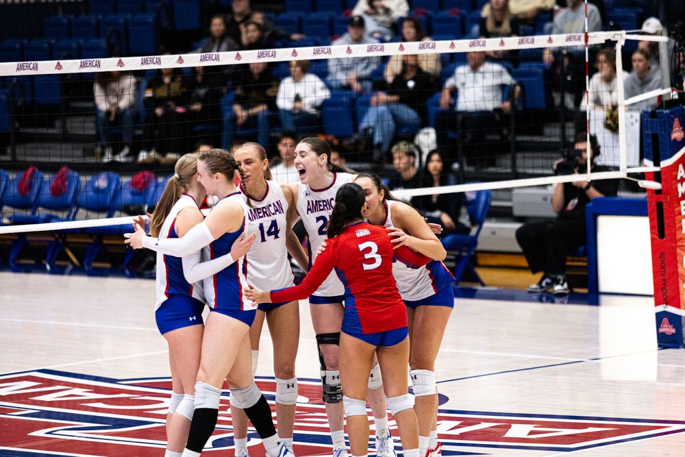 Volleyball players huddle together during competitive match on court.