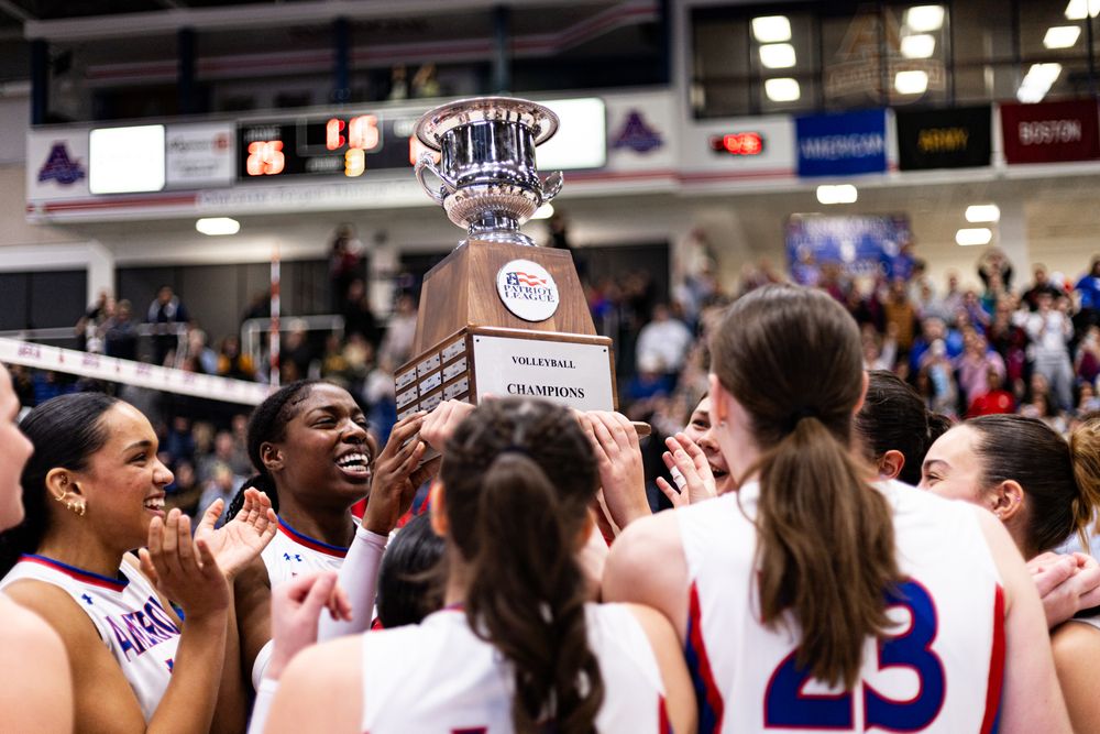 Team celebrates with championship trophy after victory in basketball arena.