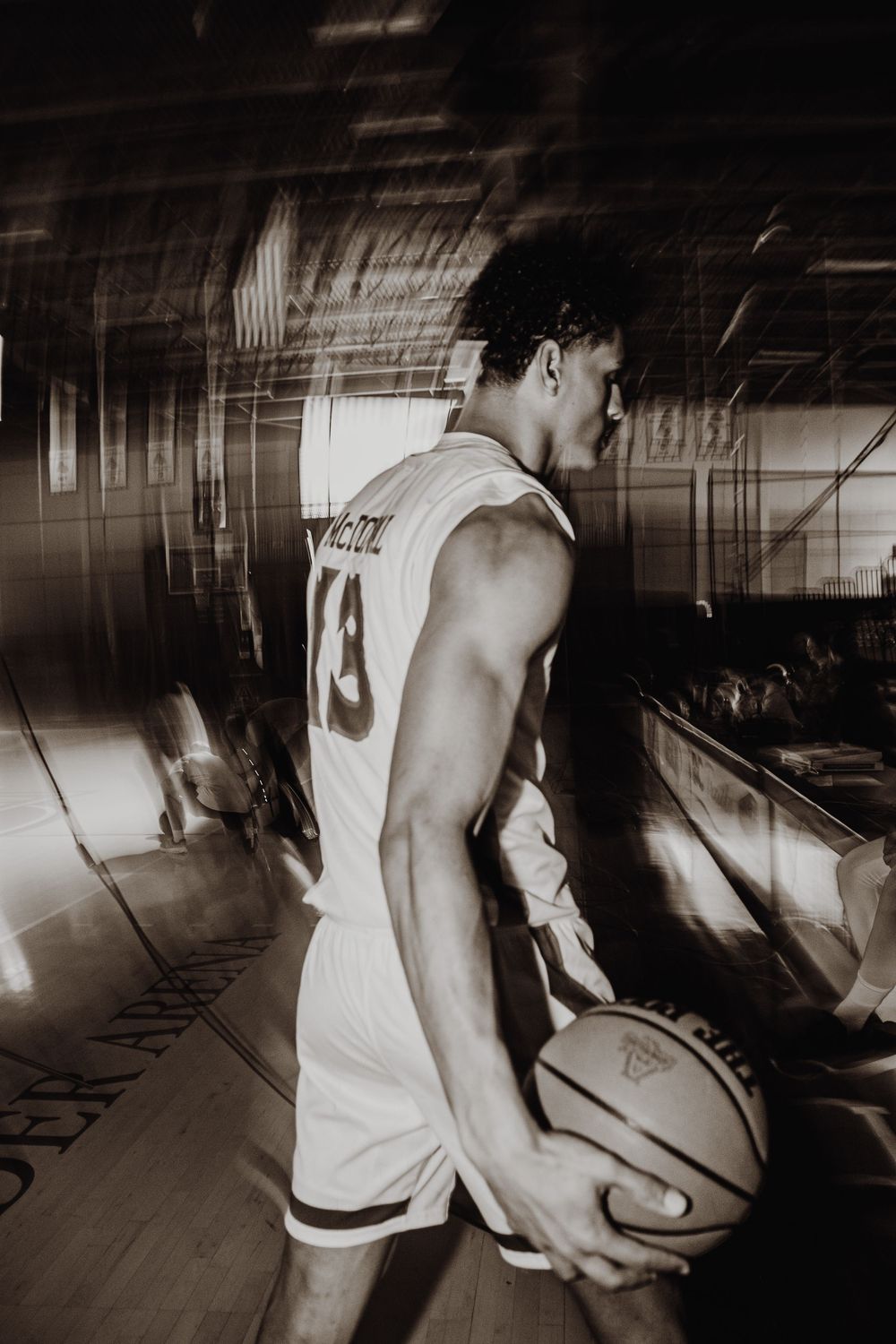 Basketball player in white jersey number 13 holds ball in dramatic black and white indoor court setting.