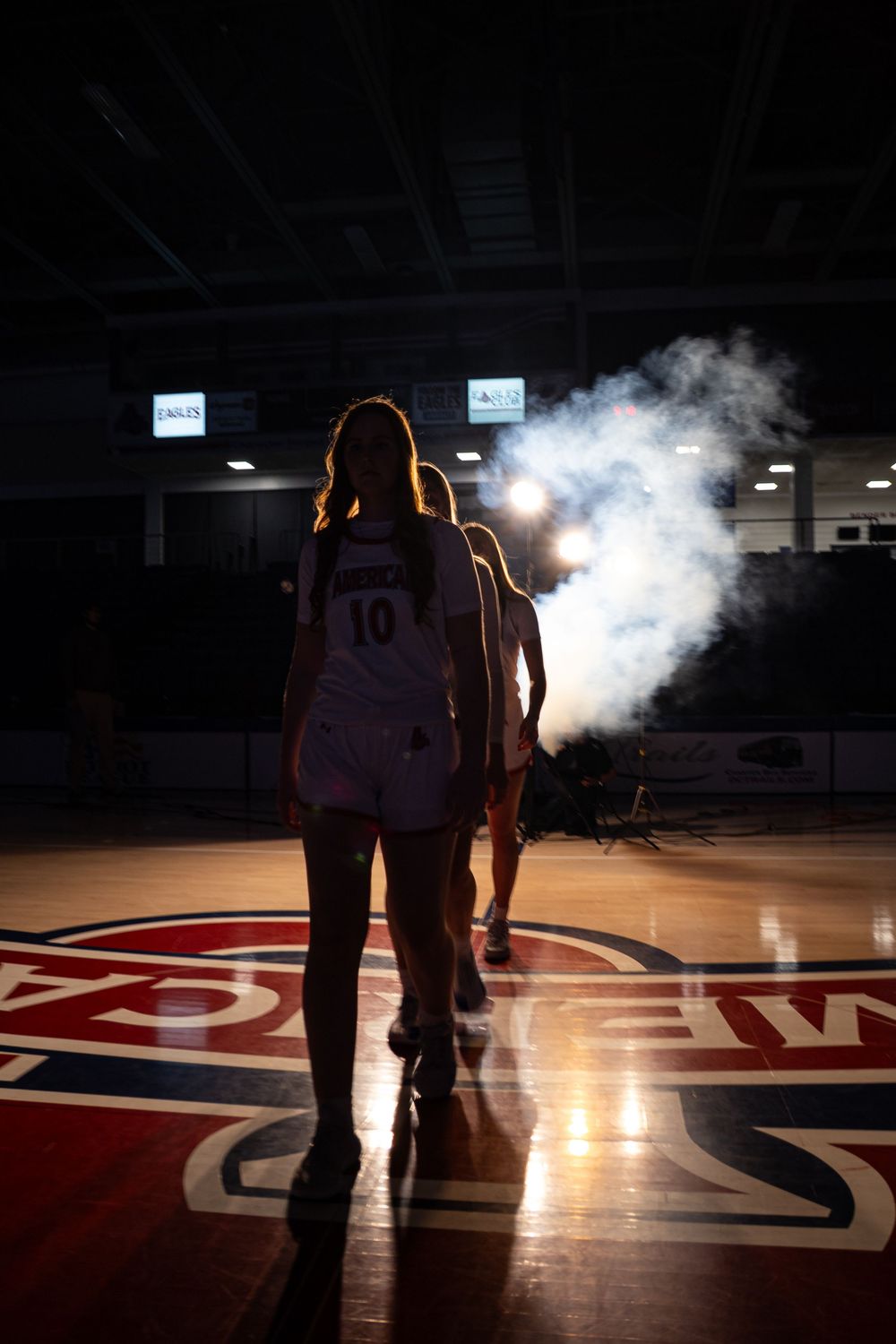Silhouetted basketball player stands in dramatic lighting with smoke effects on court.