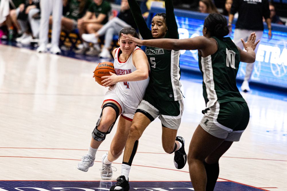 Basketball player drives to basket against defenders during intense game action.