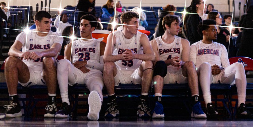Basketball players sit on bench during game break in white uniforms.