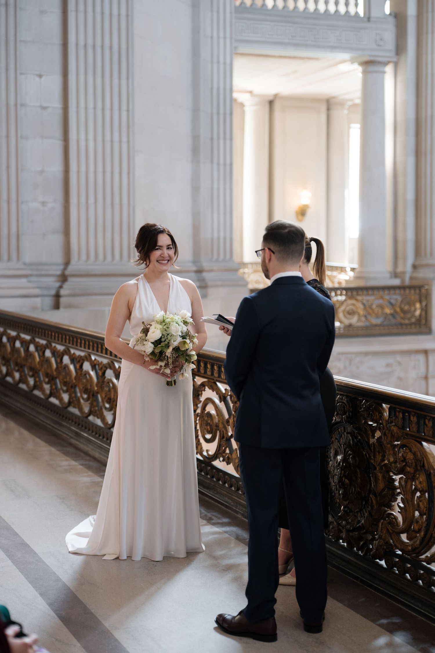 A sweet proposal moment unfolds in a grand marble hallway with ornate gold railings and classical architecture.