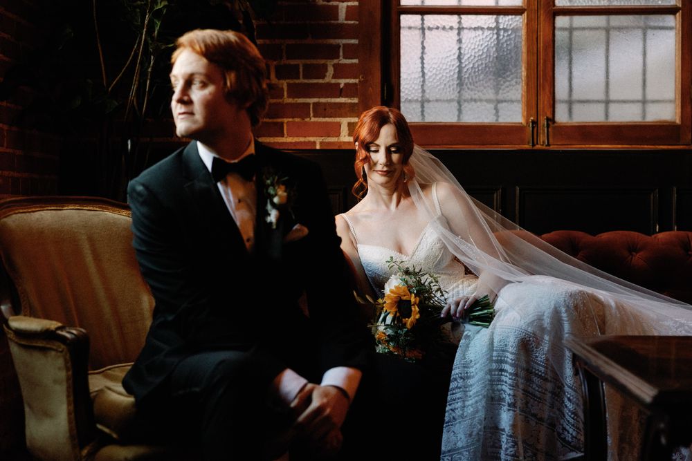 Bride and groom sitting together in a dimly lit vintage venue with brick walls and antique furniture.