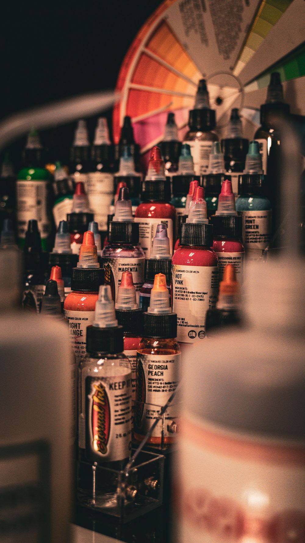 Collection of colorful tattoo ink bottles arranged on shelf in dark atmospheric lighting.