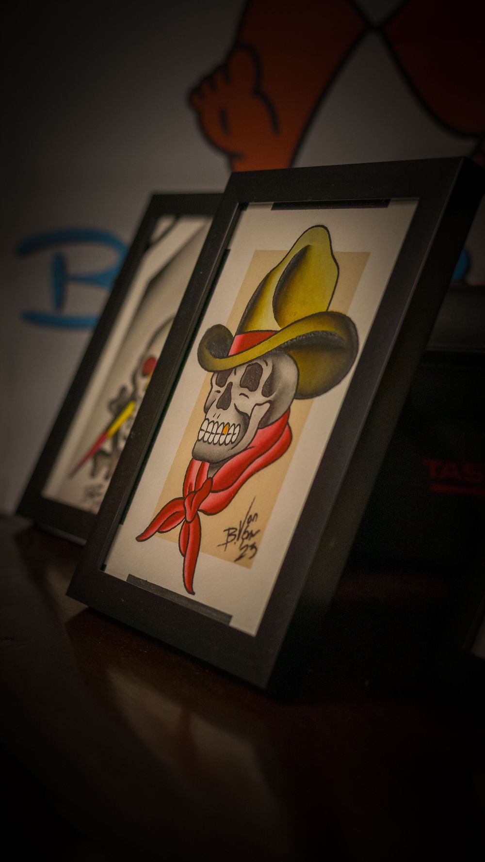 Framed artwork showing skull wearing yellow cowboy hat and red bandana in dark setting.