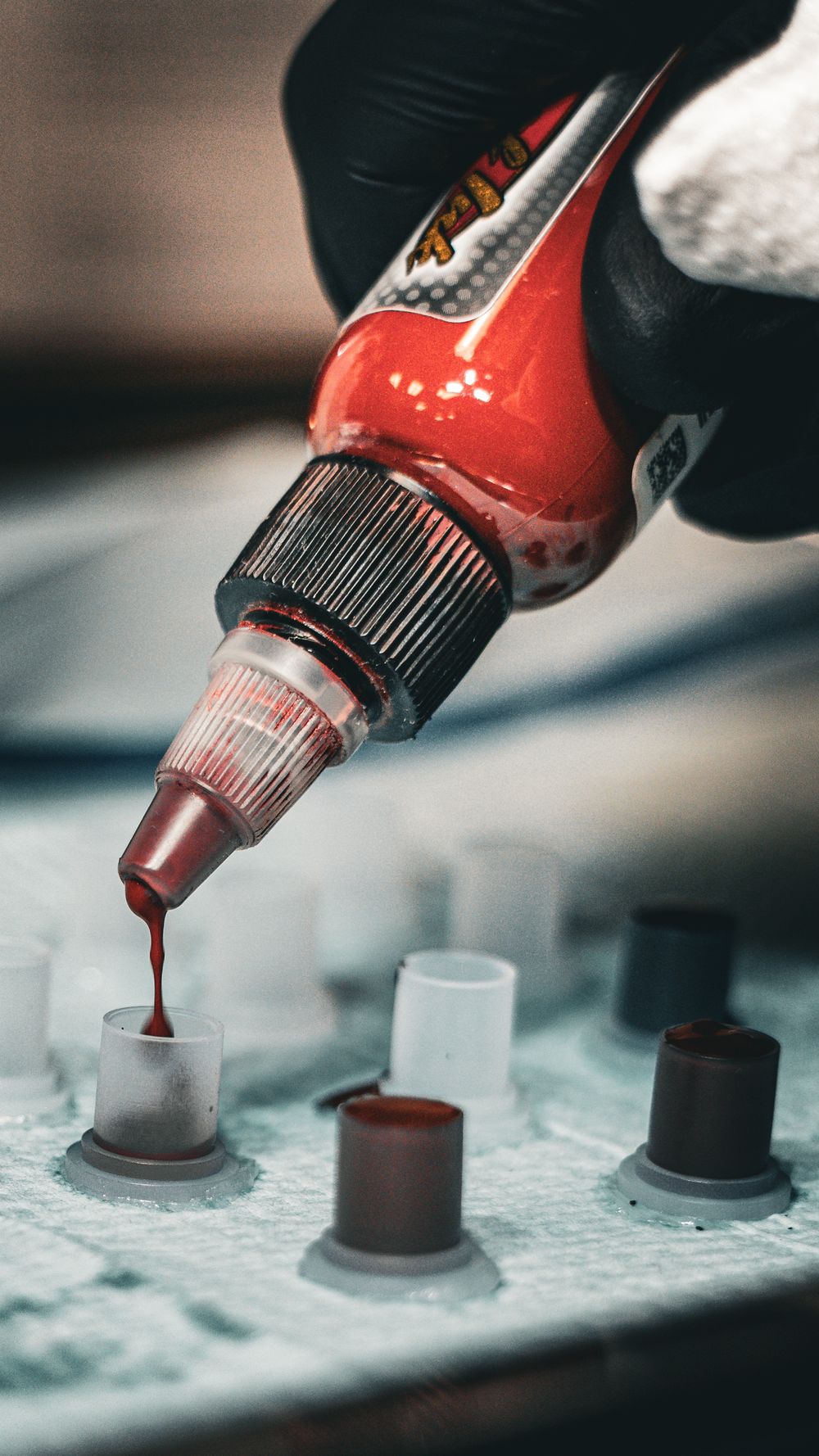 Close-up of red tattoo ink being dispensed from bottle tip in sequence.