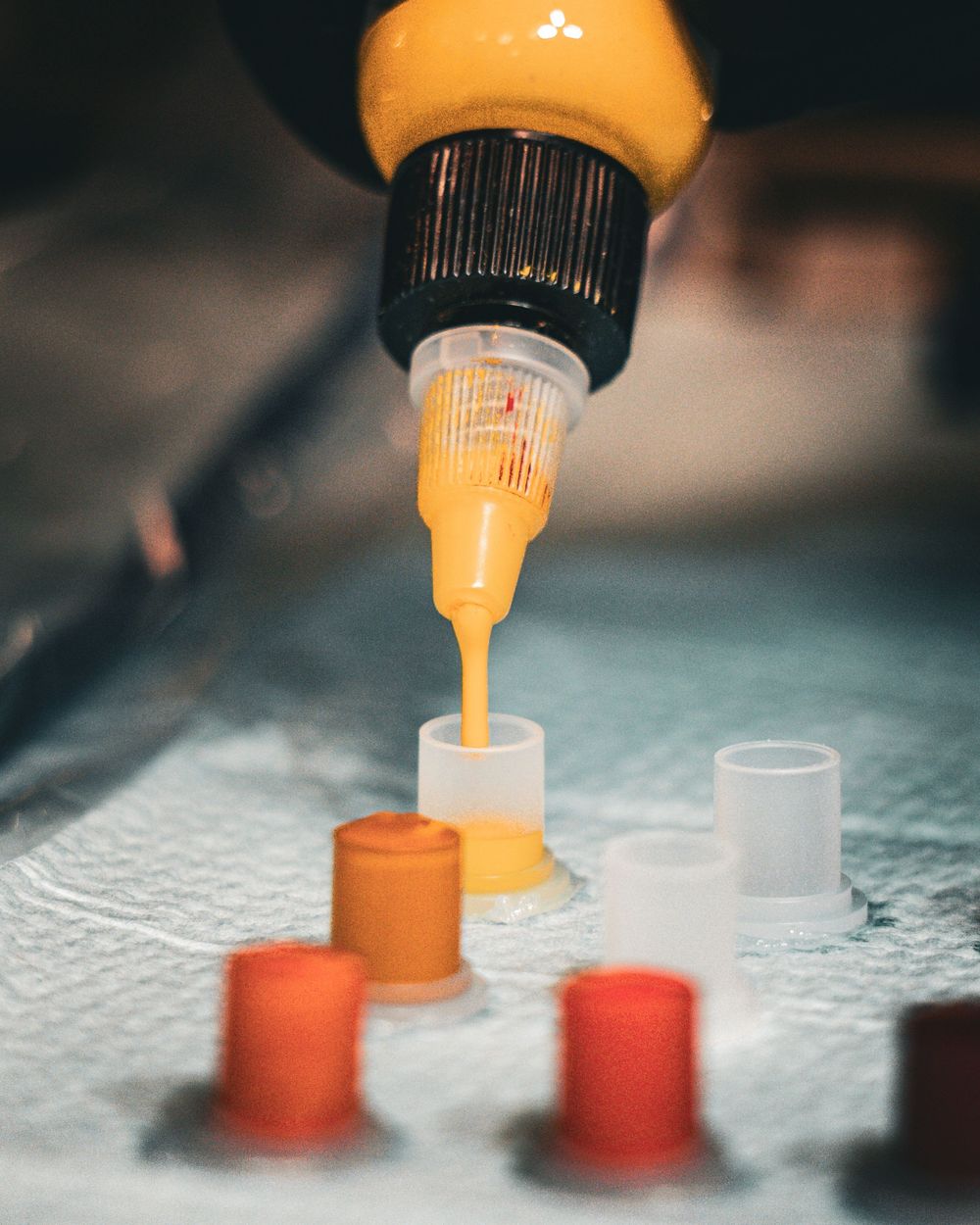 Orange ink being loaded into tattoo machine cartridges on a light surface.