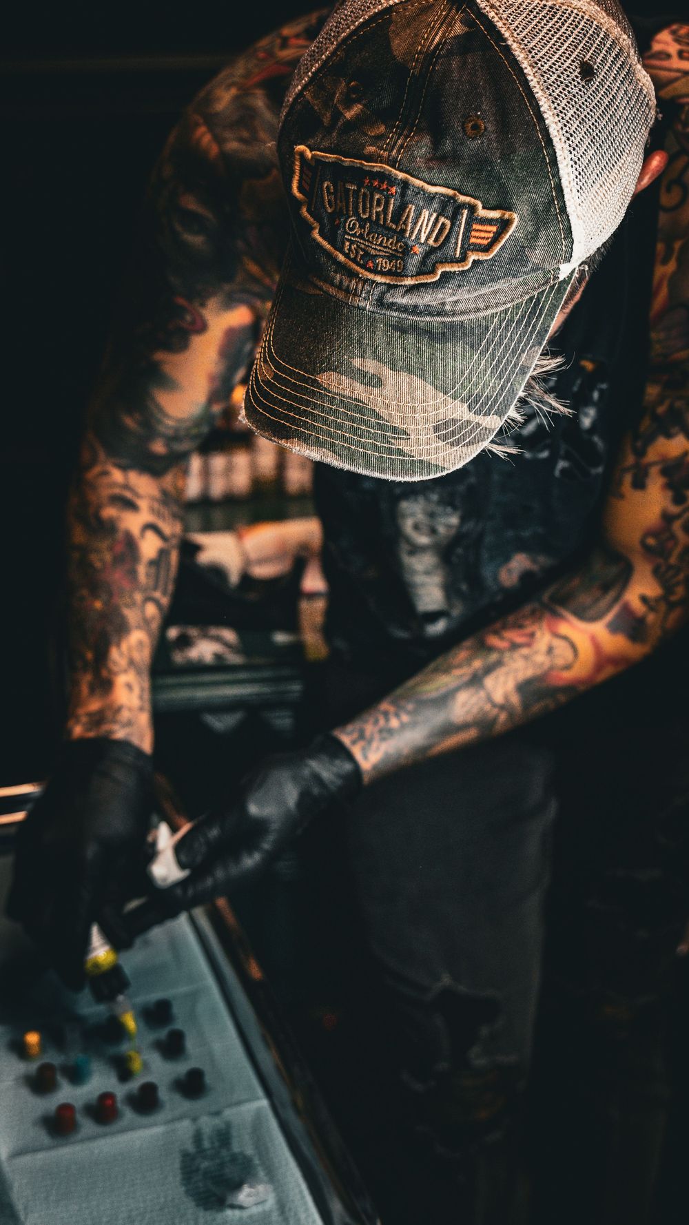Tattooed hands working with equipment in moody lighting.