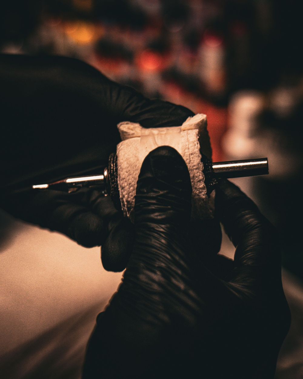 Hands wearing black gloves working with tattoo equipment in dark setting.