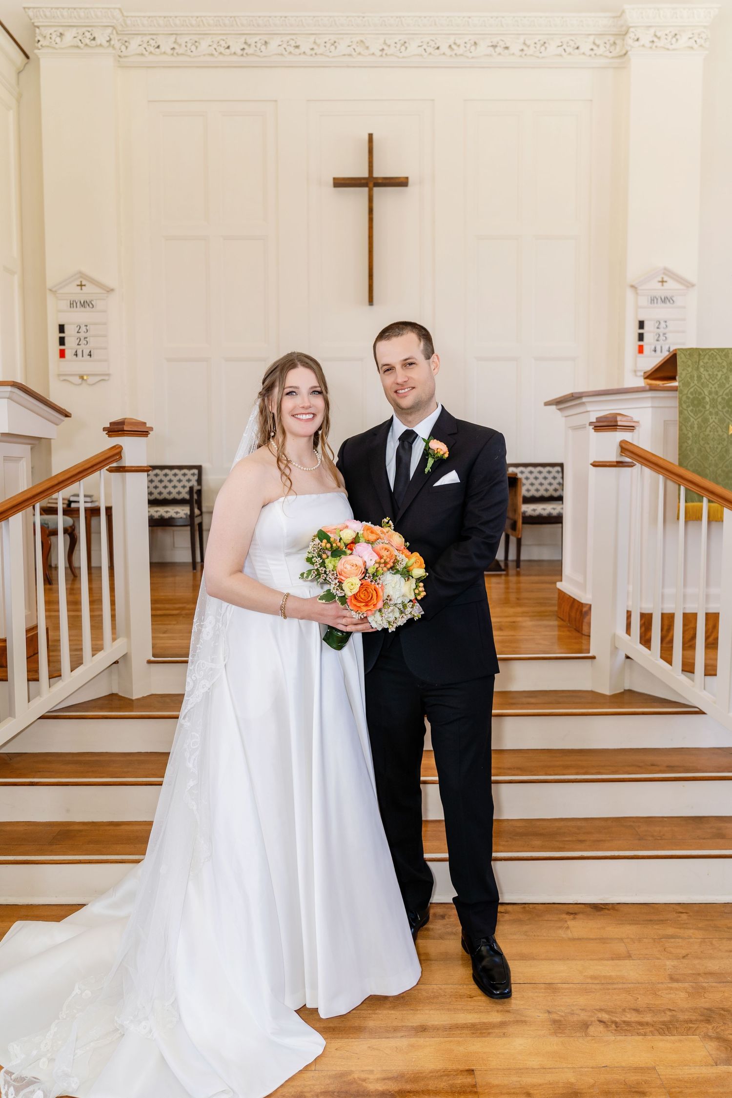 Traditional wedding ceremony takes place in a bright church sanctuary with ornate chandeliers and floral arrangements.