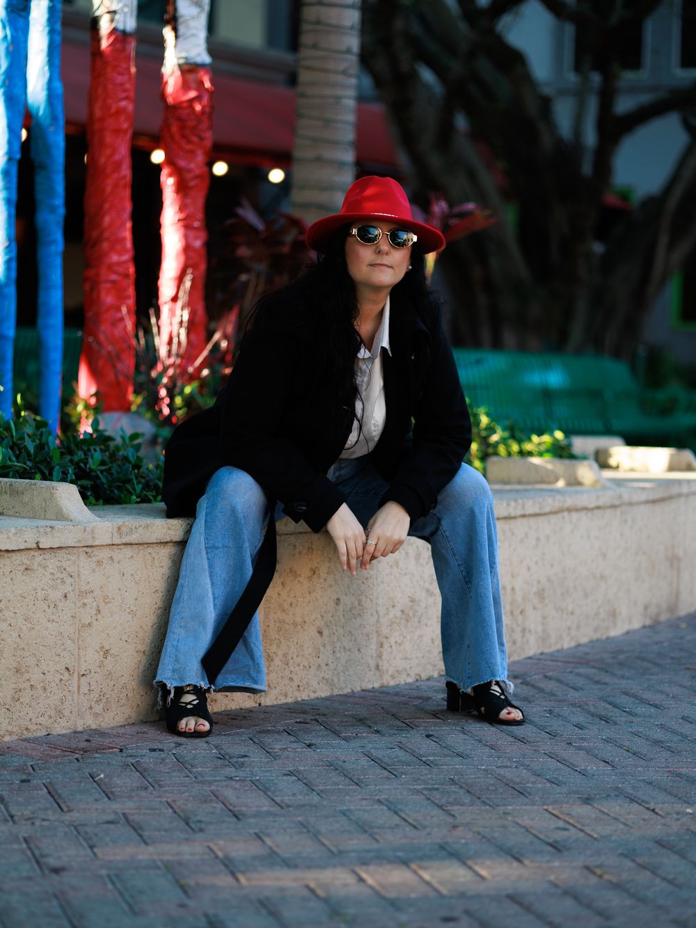 Someone sitting on a stone ledge wearing blue jeans and black sandals.