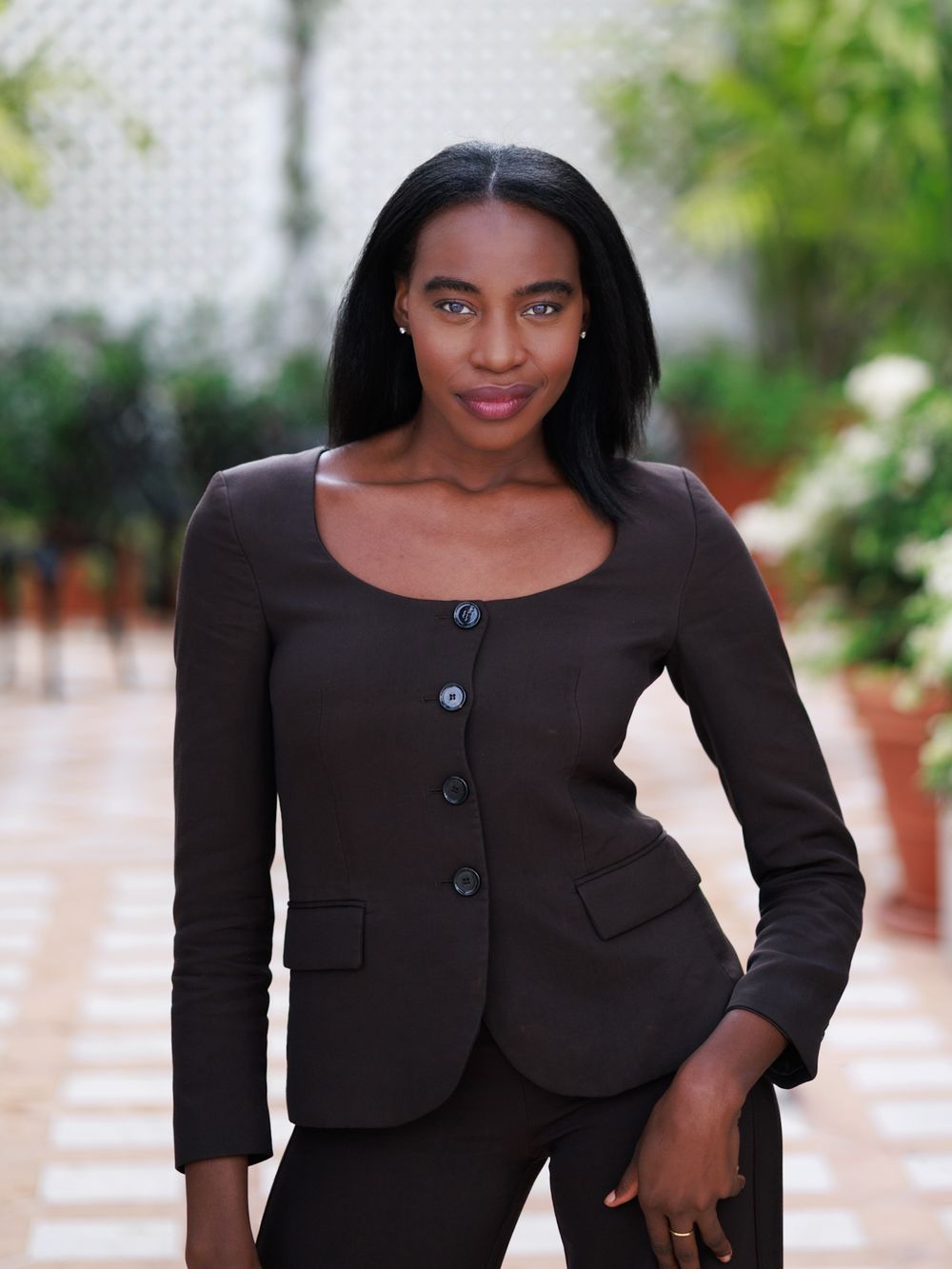 Confident Black woman in dark blazer posing indoors with elegant professional style.