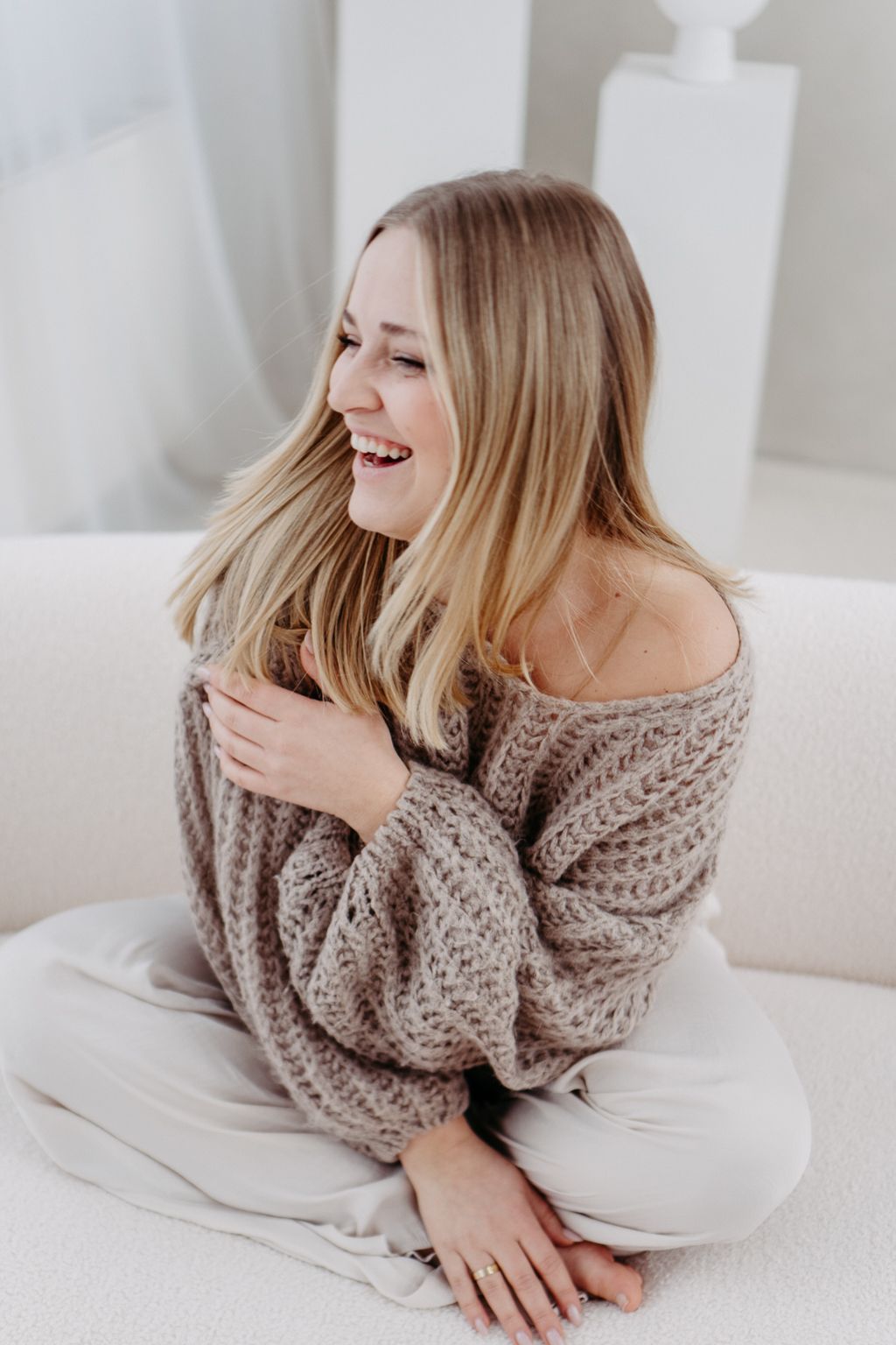 A candid lifestyle portrait of someone laughing while wearing a cozy knit sweater.