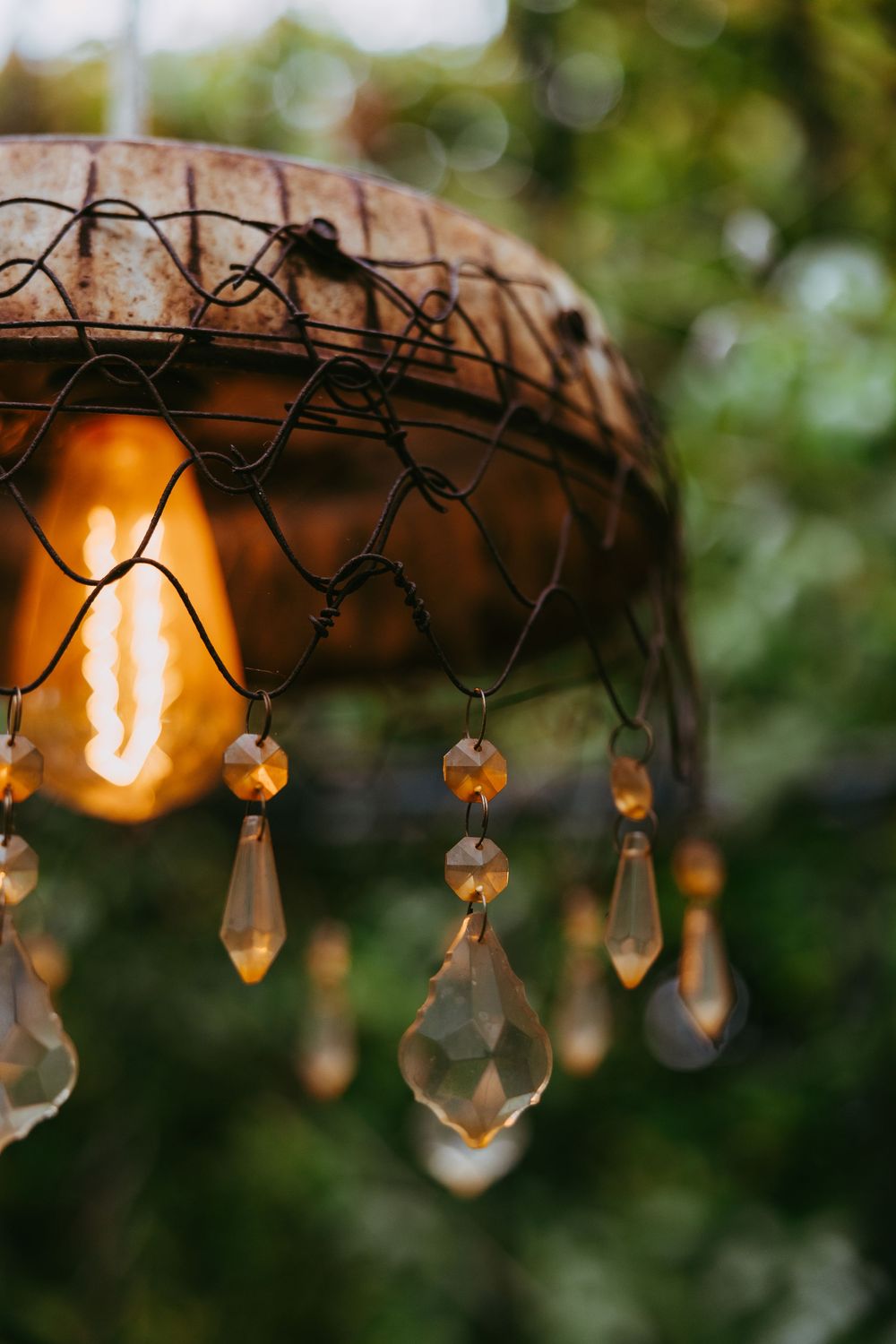 Crystal prisms hanging from a decorative light fixture create a warm, bokeh effect against blurred green foliage background.