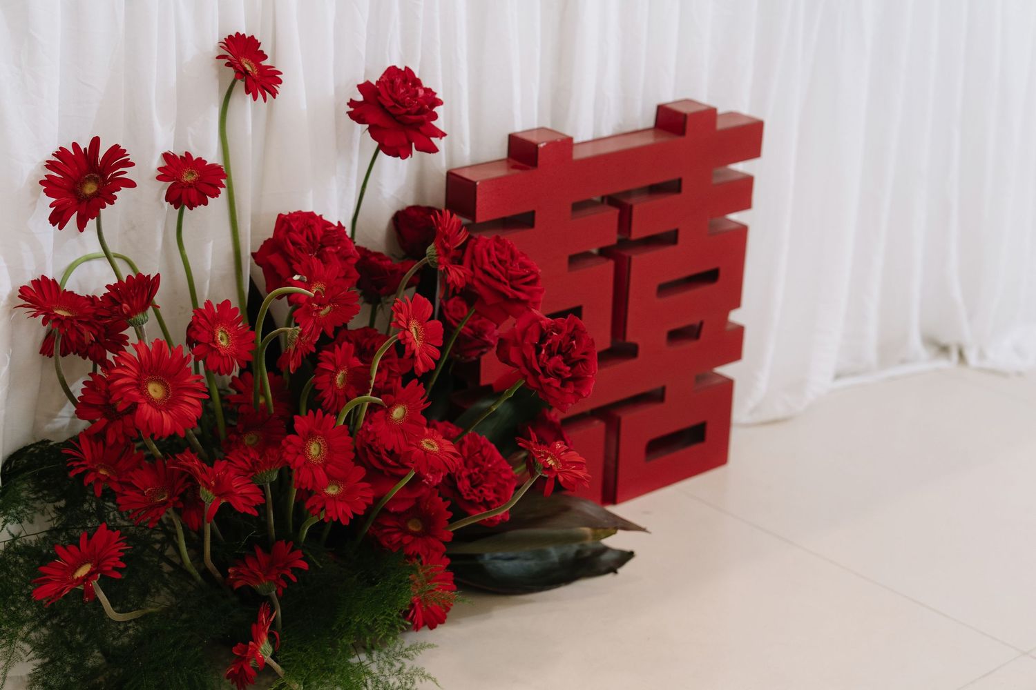 Red double happiness symbol with vibrant red gerbera daisy floral arrangement on white background.