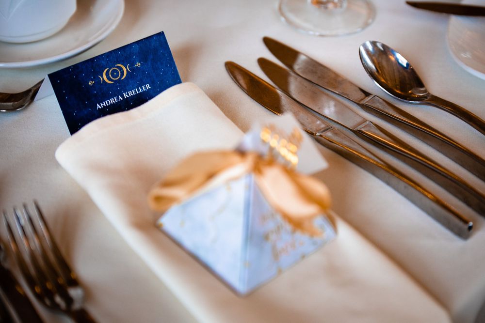 Place settings at an upscale restaurant with elegant silverware, white linens and a navy blue menu card.