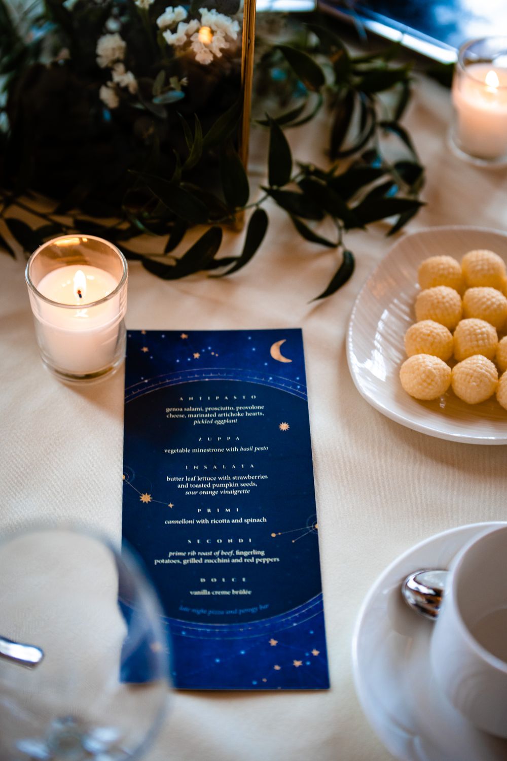 Elegant navy blue wedding menus with celestial moon and stars design displayed on white tablecloth next to candles.