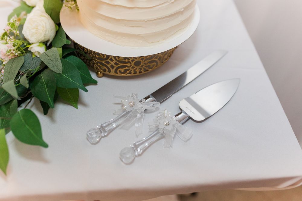 Elegant place setting with white plates, crystal glasses, and fresh green foliage on white tablecloth.