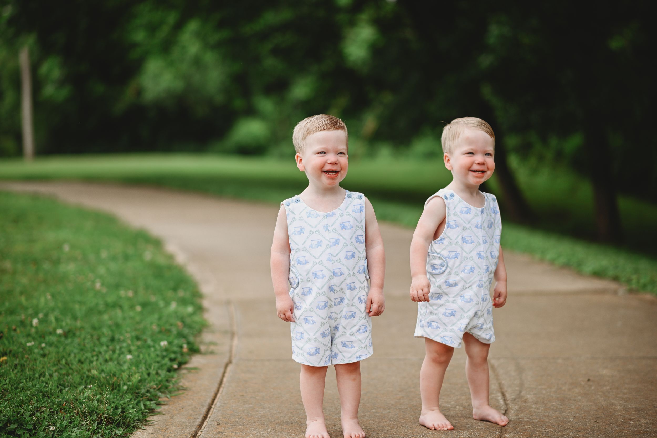 Two toddlers in matching outfits walk along a park path.