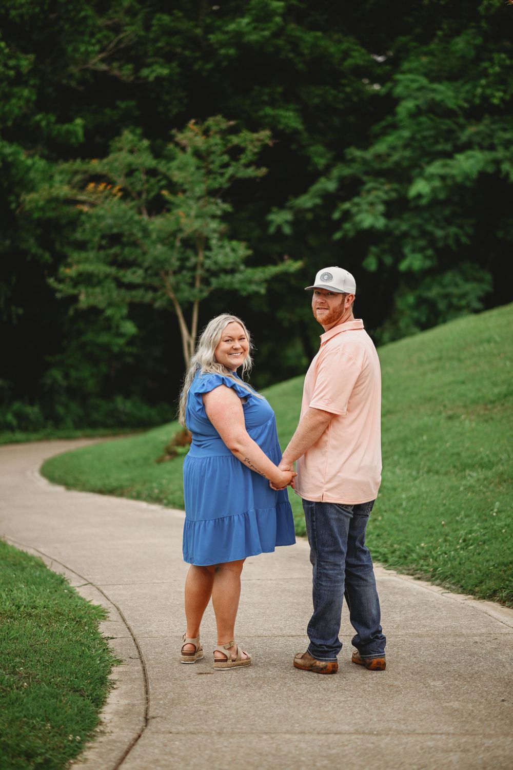 A couple holding hands on a curved pathway surrounded by lush greenery on a summer day.