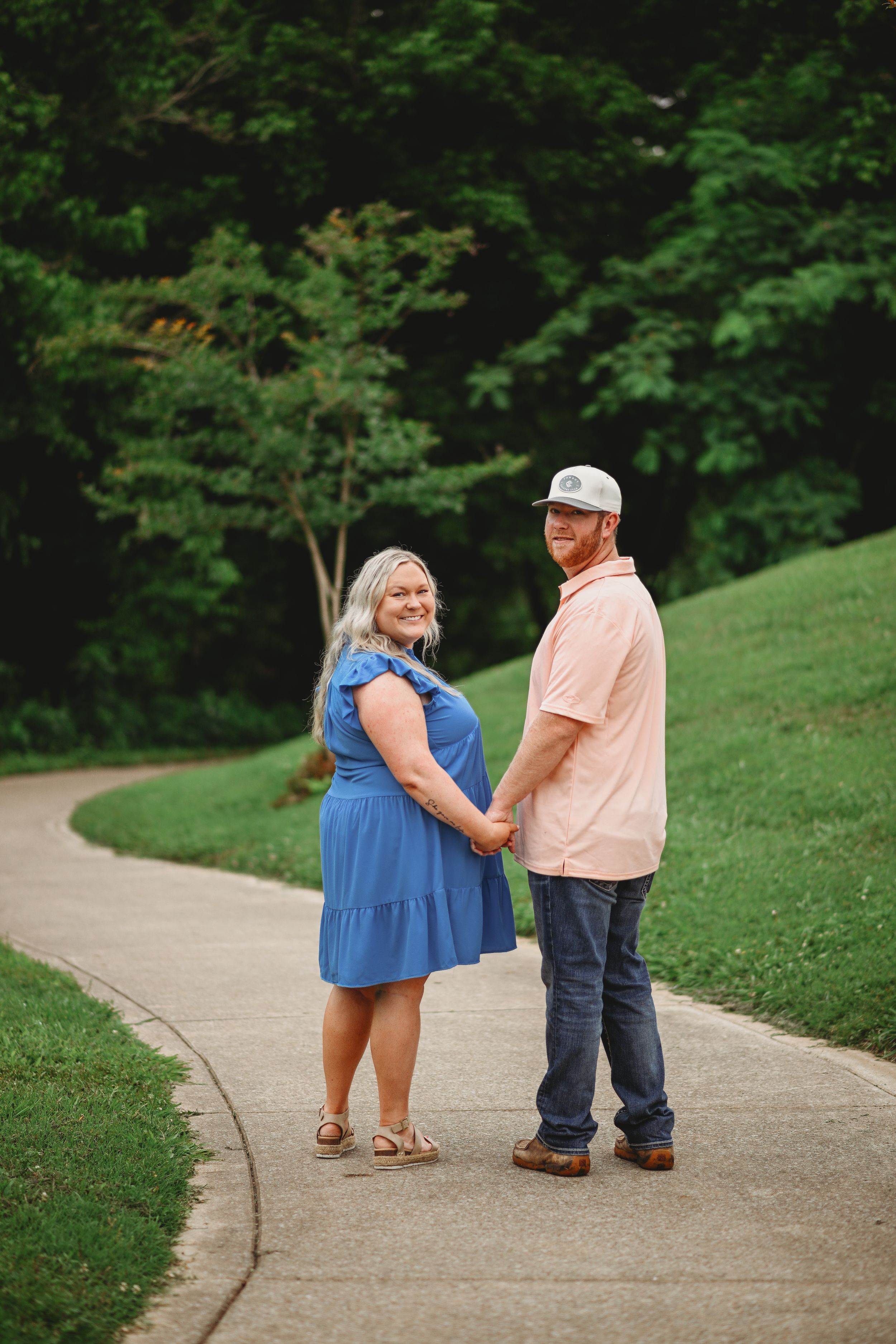 A couple holding hands on a curved pathway surrounded by lush greenery on a summer day.