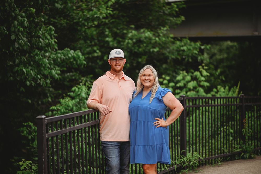 A couple posing against a metal railing with green foliage in the background.