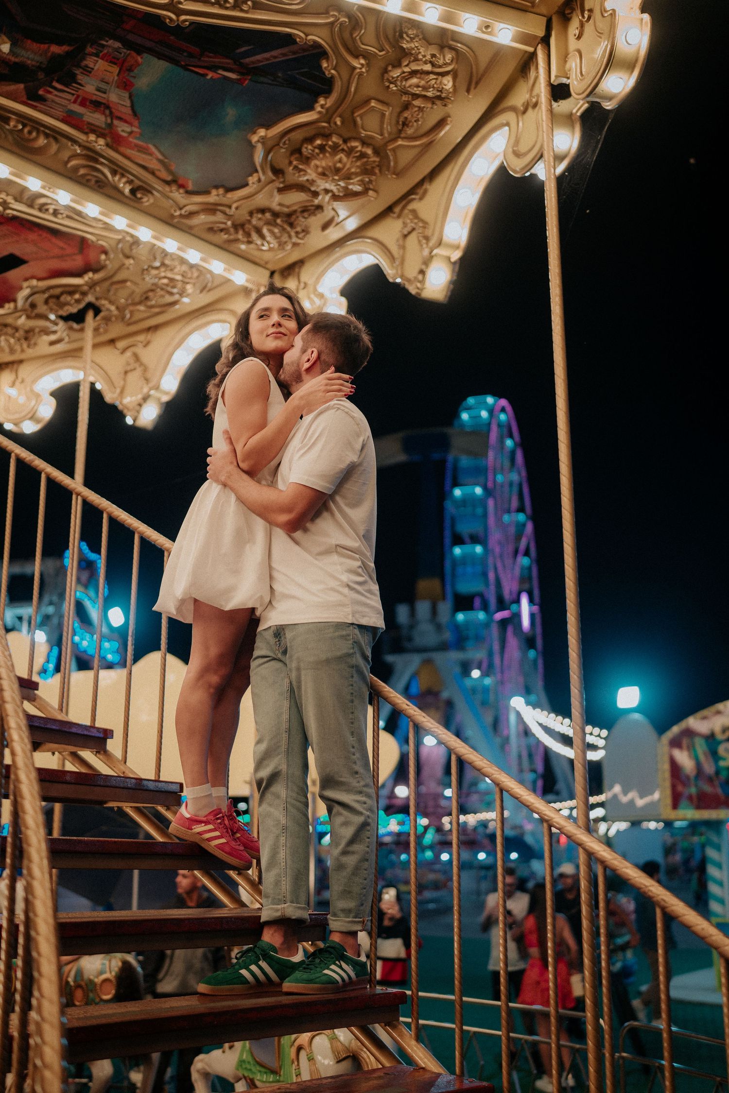Romantic nighttime scene of a couple on an illuminated carousel at an amusement park.