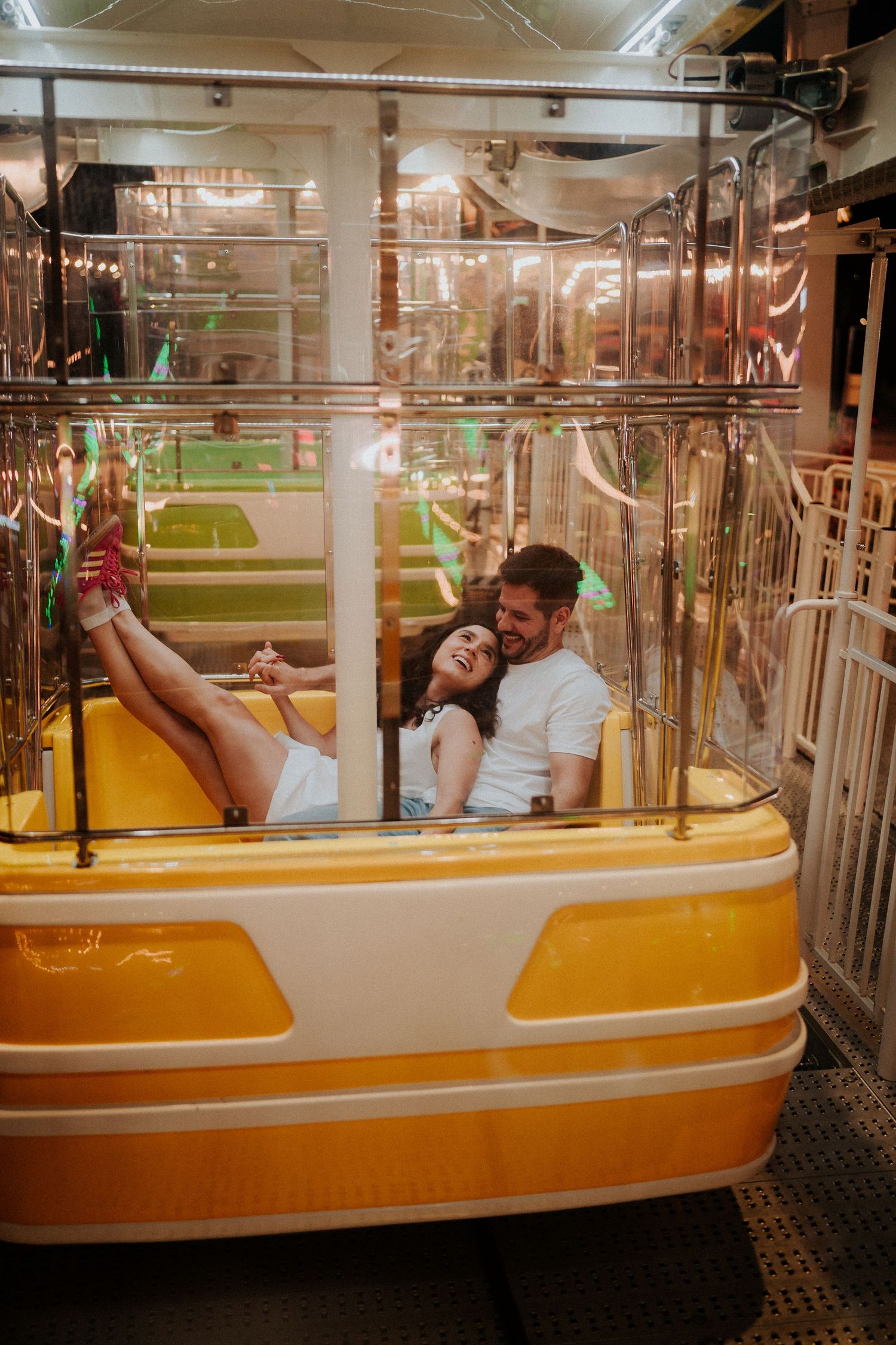 Couple enjoying playful moments in a vintage amusement park ride with orange seating.