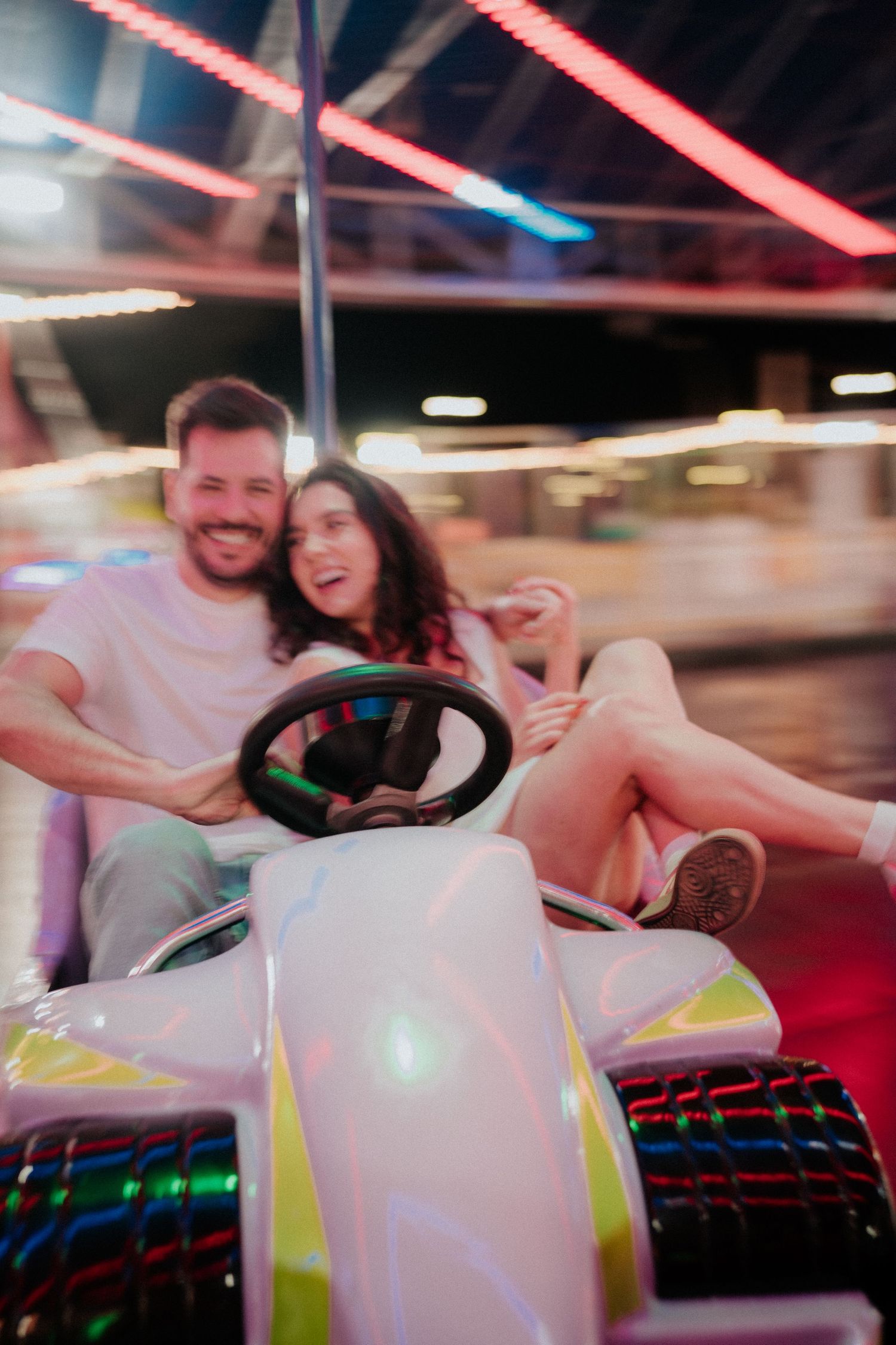 Couple enjoying a festive ride under colorful neon lights at an amusement park.