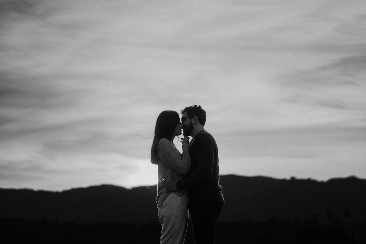 Romantic silhouette of couple embracing against cloudy sunset sky.