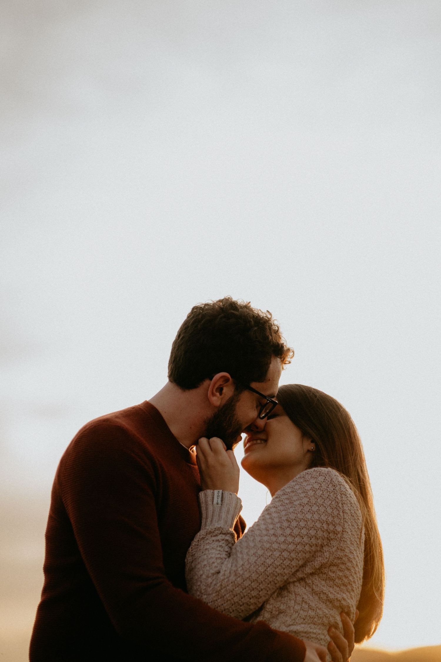 Couple in warm sweaters share tender moment during golden hour portrait session.