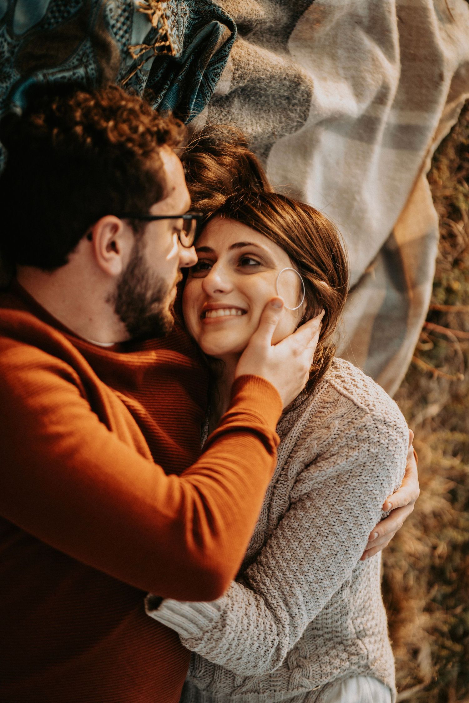 Couple wearing orange and grey sweaters embrace intimately during golden hour photoshoot.