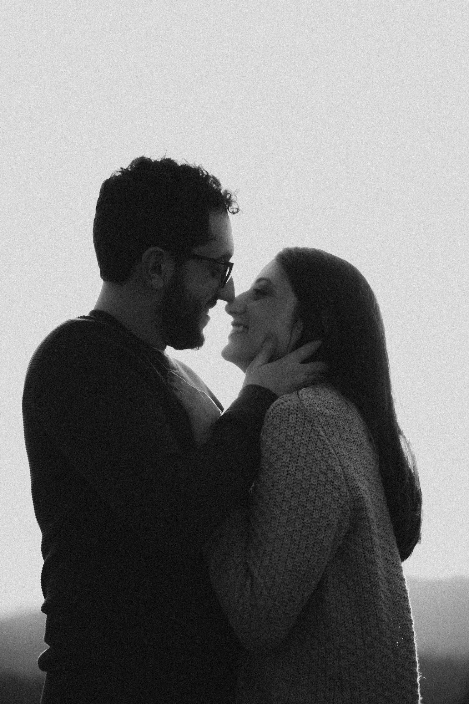 Silhouetted couple share tender moment against overcast sky.