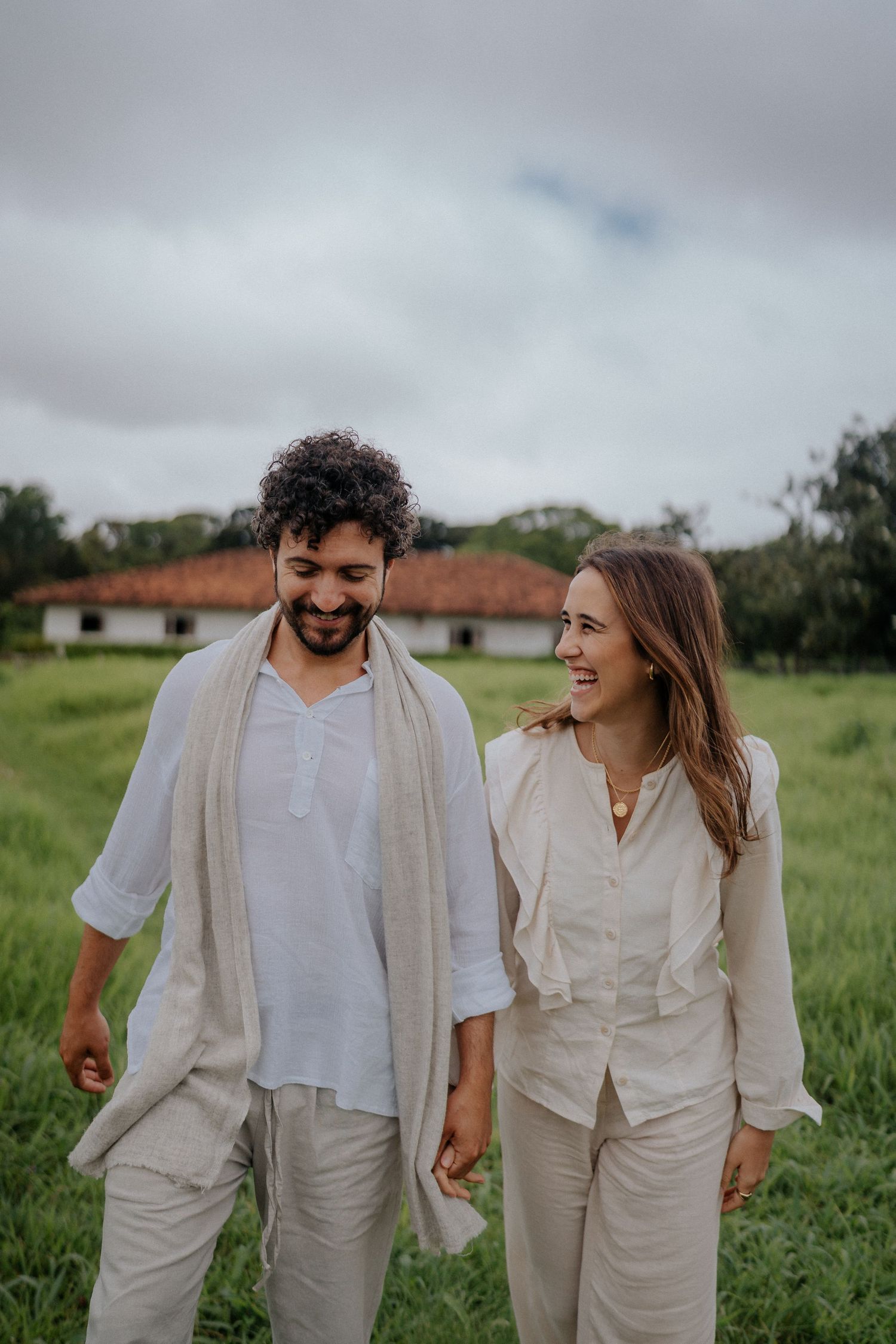 Happy couple in light colored clothing walking together in grassy field.