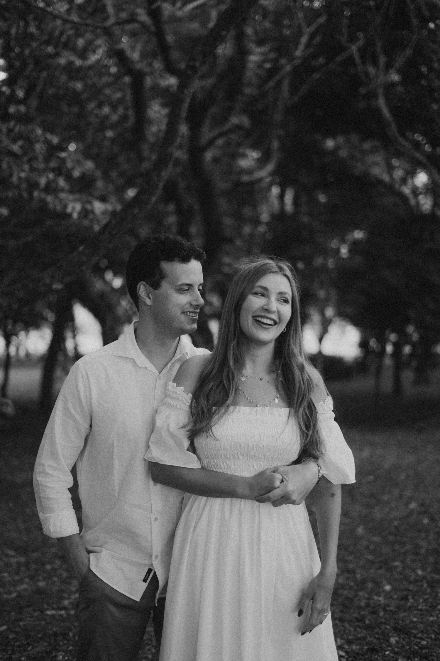 A black and white photo of a laughing couple in white clothing outdoors.