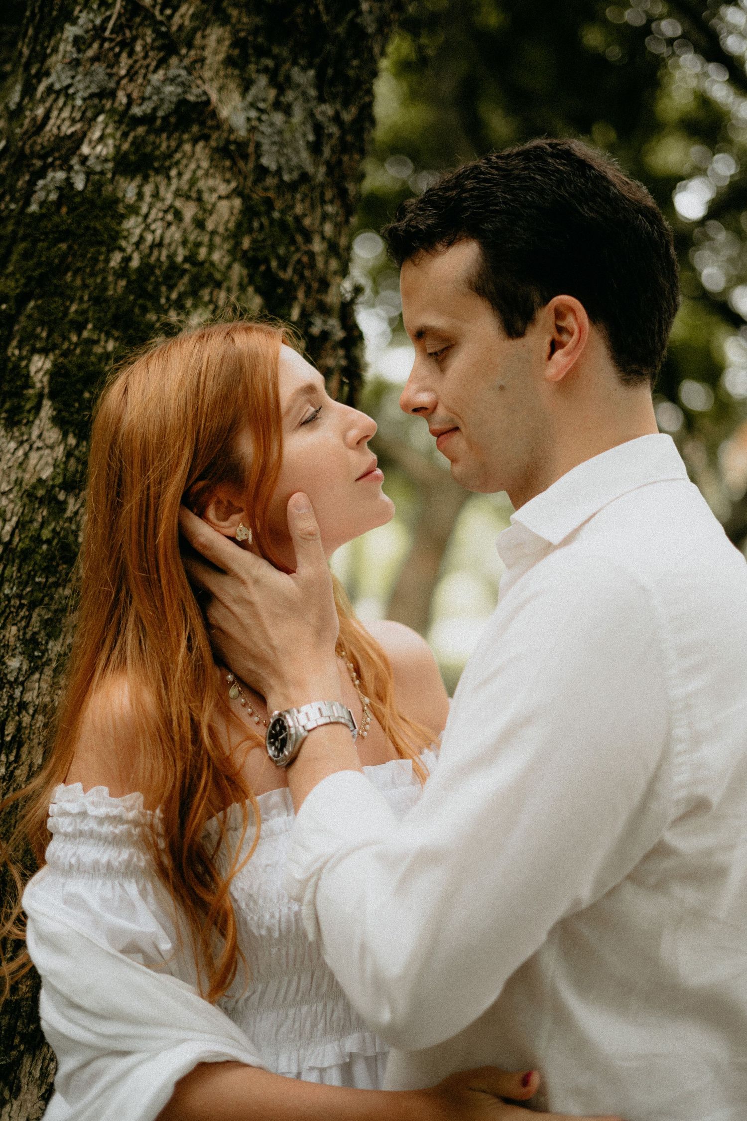 A romantic couple shares an intimate moment against a tree trunk.