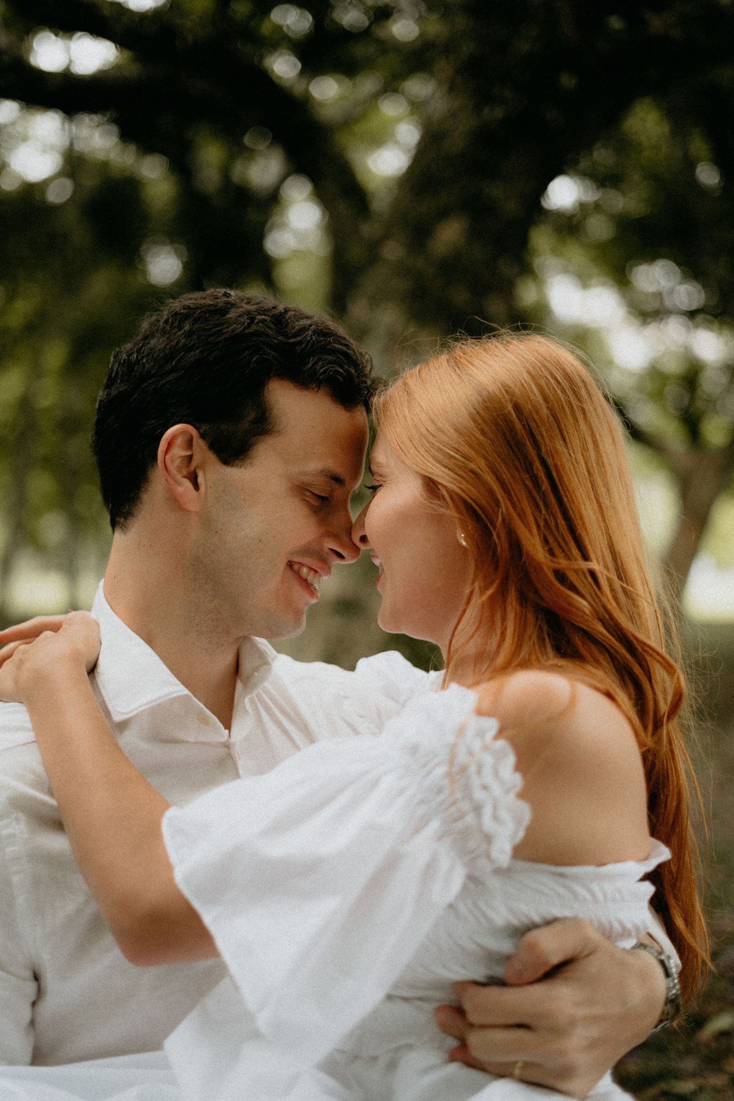 A couple in white clothing shares a tender moment in a sunlit park.